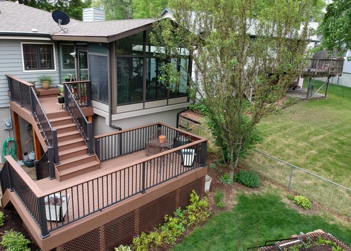 Terrasse extérieure surélevée en bois composite avec garde-corps métallique noir, escalier d'accès et véranda vitrée attenante à maison résidentielle