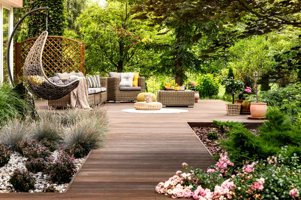Terrasse extérieure surélevée en bois composite avec garde-corps métallique noir, escalier d'accès et véranda vitrée attenante à maison résidentielle